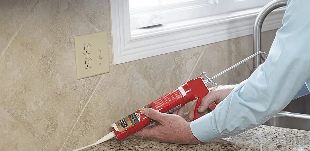 Handyman applying caulk along a kitchen backsplash and countertop seam in Providence, RI