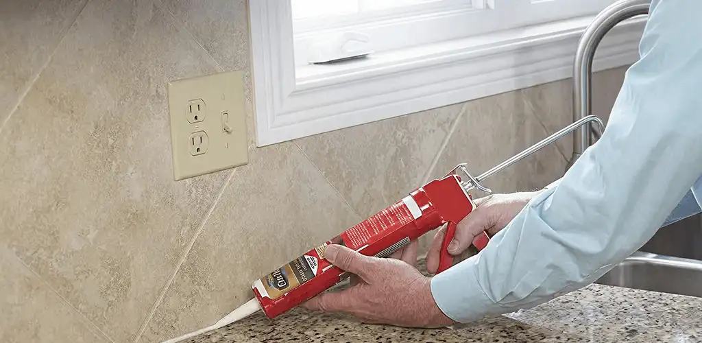 Handyman applying caulk along a kitchen backsplash and countertop seam in Providence, RI